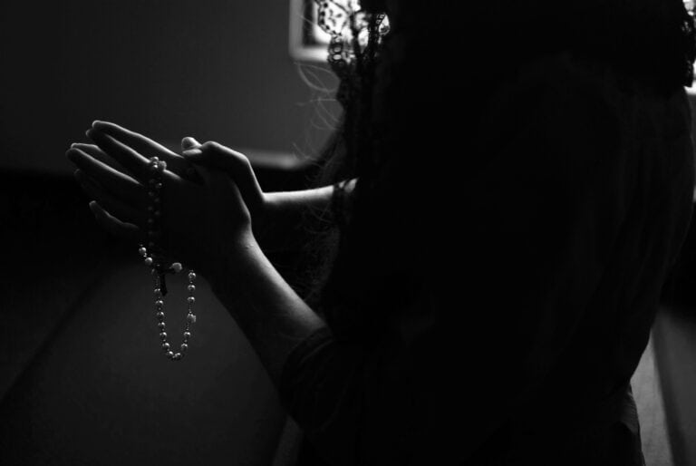 Dark silhouette of a woman prayer with a rosary between prayerful hands